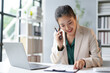 © Crystal - Businesswoman smiling while talking on the phone and pointing at documents during her workday at the office
