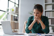 © Crystal - Young businesswoman is holding her hands together in front of her mouth, looking worried while working at her desk