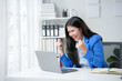 © Crystal - Asian businesswoman is raising her fists in front of her laptop, happy about her achievements