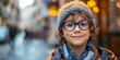 © inspiretta - A young boy wearing glasses and a hat is smiling. He is standing on a street with other people around him