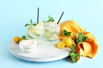 Board and glasses with fresh lemonade on blue background