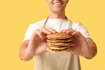 Wall Mural - Young man with tasty homemade pancakes on yellow background, closeup