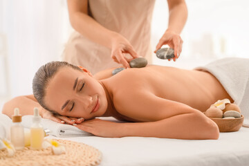 Poster - Young woman having massage with hot stones in spa salon