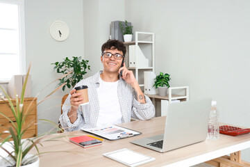 Wall Mural - Male accountant in eyeglasses talking with mobile phone and holding cup of coffee at workplace in office