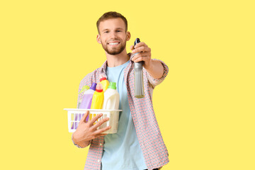 Poster - Male janitor holding basket with cleaning supplies on yellow background