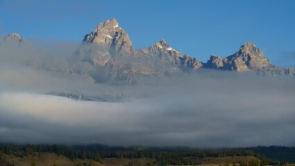 Wall Mural - Grand Teton mountain range with low-lying clouds and a clear blue sky in Teton County, Wyoming, USA