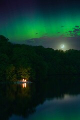 Wall Mural - Vertical view of a night landscape with a campfire by a lake, under a green aurora borealis