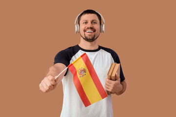 Poster - Handsome man in headphones with flag of Spain and books on brown background