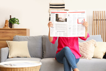 Poster - Woman with newspaper sitting on sofa at home