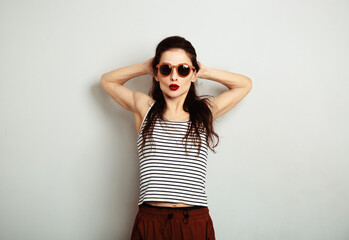 Wall Mural - Fun relax smiling woman posing in fashion sunglasses and stripped t-shirt with red lipstick on white wall background with empty copy space. Happy fashion lifestyle