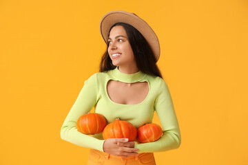 Wall Mural - Beautiful young woman with fresh pumpkins on yellow background