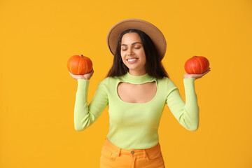 Wall Mural - Beautiful young woman with fresh pumpkins on yellow background