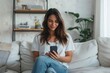 © evgenia_lo - A young Caucasian woman smiles as she uses her smartphone, comfortably seated on a sofa in a cozy living room.