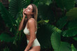 © blackday - Young woman with wet hair wearing bikini surrounded by lush tropical leaves
