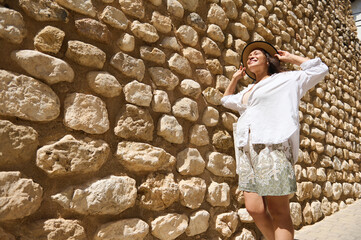 Cheerful woman enjoying the sunny day against a rustic stone wall