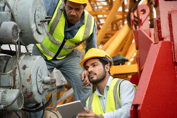 Two Asia engineers man worker checking machine and use tablet computer with spare crane background	