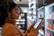 © john - Black female customer using a digital screen to browse cosmetic products in a modern store.