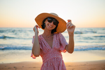 Wall Mural - Portrait of a happy girl in a dress and hat enjoying her summer vacation on the beach.