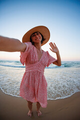 Wall Mural - Portrait of a beautiful young woman in a hat on the seashore. Cheerful young woman smiling on the beach during summer vacation.