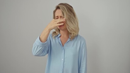 Poster - Disgusted young blonde woman holding breath, pinching nose against atrocious stink, standing isolated on white background. wearing shirt, her expression screams intolerable, repugnant smell.