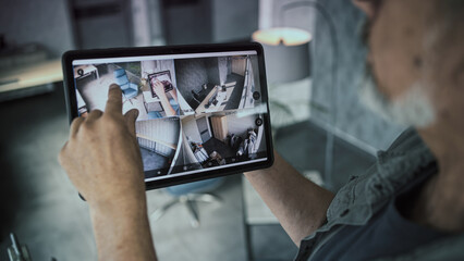 Male mature technician watches and controls CCTV cameras in modern office using tablet computer. Tablet screen shows security cameras footage. Monitoring and tracking. Surveillance system and privacy.