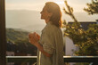 © olezzo - Young woman greeting the morning and sunrise standing on a balcony overlooking the mountains