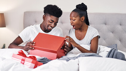 Anniversary, box and surprise with black couple in bedroom of home together for bonding or celebration. Gift, romance or wow with happy African man and woman in bed for birthday or valentines day