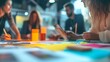 © Prostock-studio - A diverse team collaborates at a table covered with colorful papers and tools, focusing on ideas and sketches in a contemporary workspace.