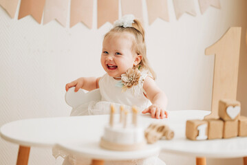 Wall Mural - Cute beautiful girl baby sitting on the chair in the children's room and playing in eco wooden toys cubes and pyramid. First birthday party happy and cheerful