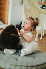 Wall Mural - Cute beautiful girl baby sitting on the floor in the children's room and playing in eco soft plush toys