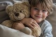 © ChaoticMind - A young boy with freckles happily hugs his teddy bear while sitting comfortably on the couch, capturing the essence of childhood joy, warmth, and innocence.