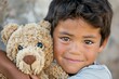 © ChaoticMind - A happy young boy outside embraces a teddy bear, displaying a warm and wide smile, capturing the essence of childhood joy, innocence, and affection for a beloved toy.