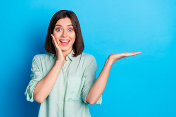 Sticker - Photo of ecstatic woman dressed turquoise shirt show product on palm empty space hand on cheekbone isolated on blue color background