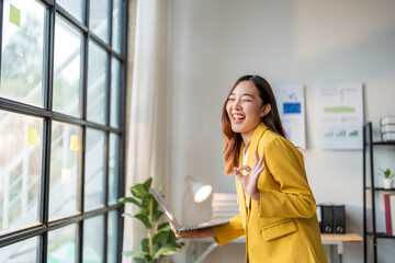 Wall Mural - young manager woman holding laptop is making ok sign and smiling in office