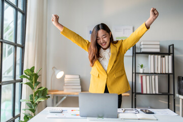 Wall Mural - happy asian businesswoman celebrating success raising arms working from home office
