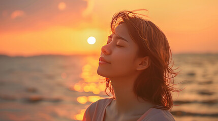 Wall Mural - Young woman standing by the sea at sunset, eyes closed, expressing pure delight and calmness