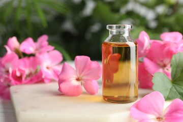 Wall Mural - Bottle of geranium essential oil and beautiful flowers on white table, closeup