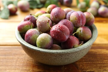 Wall Mural - Ripe plums in bowl on wooden table, closeup