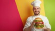 © Maria Mikhaylichenko - Cheerful chef in white uniform and hat proudly presenting a large, appetizing burger against a vibrant multicolored background of pink, yellow, and green.
