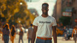© Игорь Зубченко - A man in a white 'Volunteer' t-shirt , with a brown belt, stands against a high-resolution street background. The focus is on him, with blurred people and good lighting.