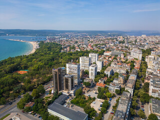 Aerial view of a coastal city with a mix of urban development, lush greenery, and a sandy beach. The expansive panorama showcases the vibrant life and natural beauty of the area. Bulgaria, Varna.