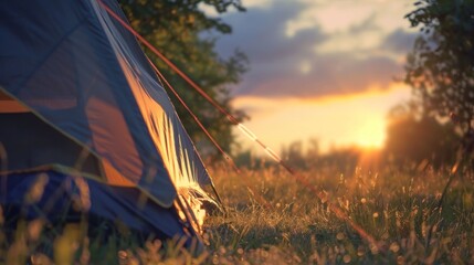 Wall Mural - Camping tent at sunset with warm light illuminating the scene and a grassy field in the foreground