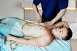 © grigvovan - Mobile massage therapist kneads chest muscles of young man lying on massage table at home.