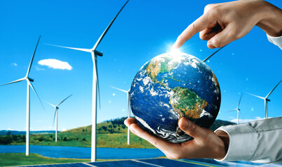 Wall Mural - Concept of sustainability development by alternative energy. Man hand take care of planet earth with environmentally friendly wind turbine farm and green renewable energy in background. uds