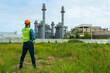 © supAVADEE BUTRADEE - Asian male engineer wearing engineering helmet stand checking work with taple and hold walkie-talkiein an oil refinery and power plant in the evening.