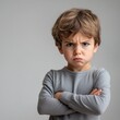 © Halina - Portrait of a young boy with a serious expression and crossed arms on a neutral background conveying frustration or stubbornness