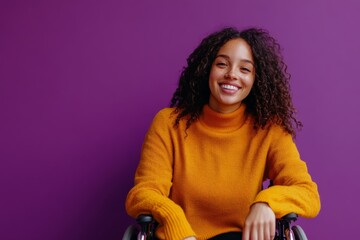 A woman in a bright orange sweater smiles widely while seated in her wheelchair against a vibrant purple wall, radiating positivity and confidence