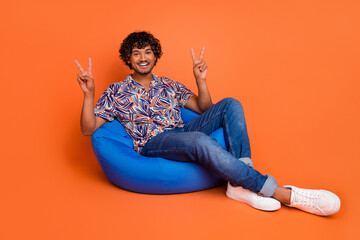 Sticker - Full body photo of attractive young man bean bag v-sign dressed stylish colorful clothes isolated on orange color background