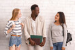 © Prostock-studio - Carefree group of multiethnic students with bags and books having conversation before university over white brick wall