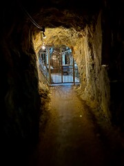 A dimly lit mine tunnel leads to a gated exit, revealing a glimpse of the world beyond the darkness. An evocative shot of confinement and the promise of freedom.